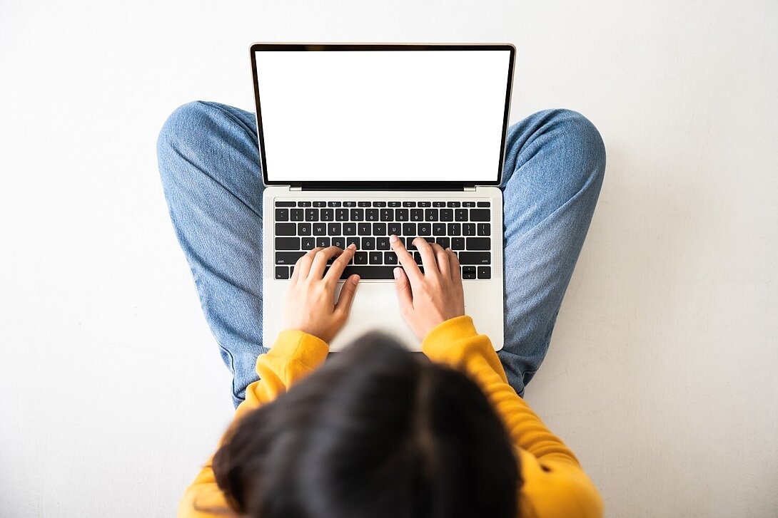 Frau sitzt auf dem Boden und hat einen Laptop auf dem Schoß