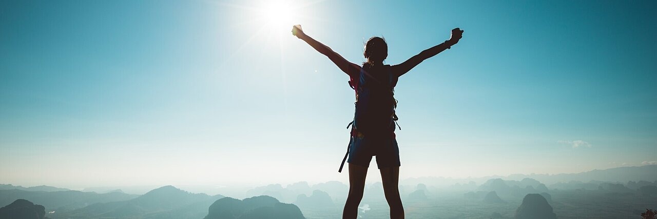 Frau mit Backpacker genießt die Aussicht auf einer Bergspitze und jubelt 