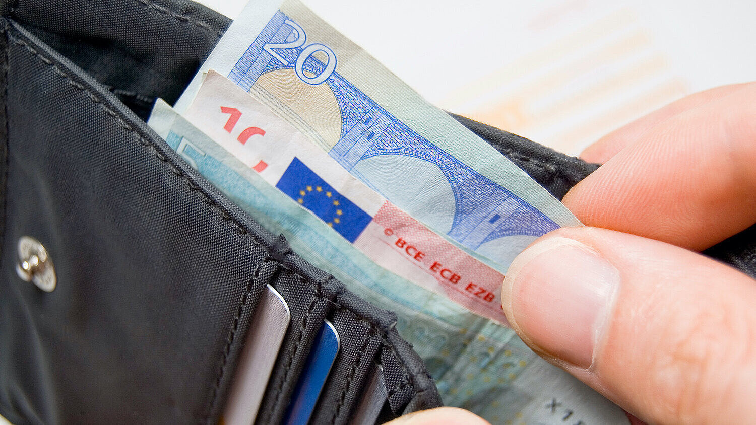Eine Person holt Geldscheine aus einem Portemonnaie 