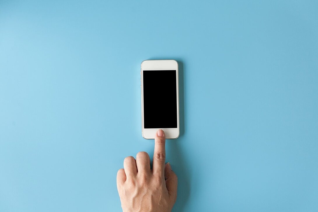 Linker Zeigefinger berührt Smartphone vor blauem Hintergrund