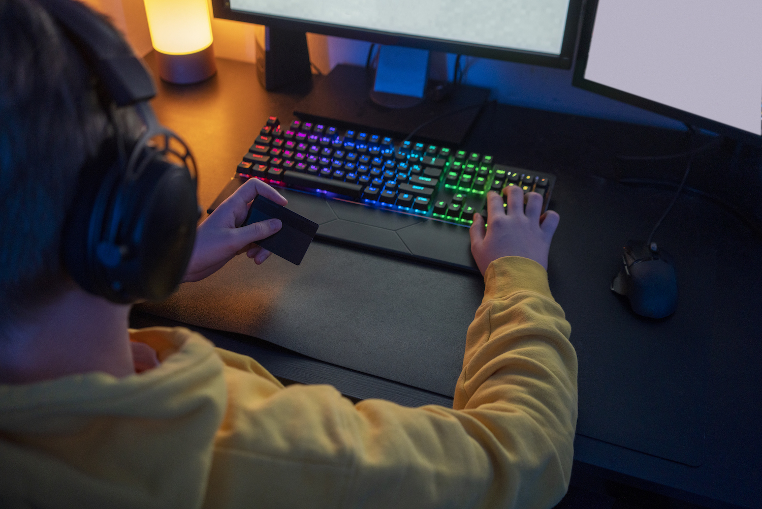 Gamer sitzt am PC und hält eine Kreditkarte in der Hand – Symbol für Gamblification und den Einfluss von Glücksspielelementen in Videospielen.